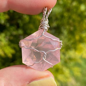 May include: A pink rose quartz crystal pendant wrapped in silver wire, forming a six-pointed star shape.