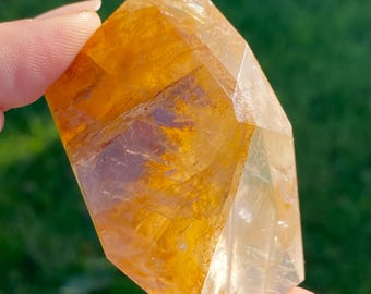 May include: A large, clear, faceted crystal with a golden yellow hue. The crystal is shaped like a point and has a smooth, polished surface.