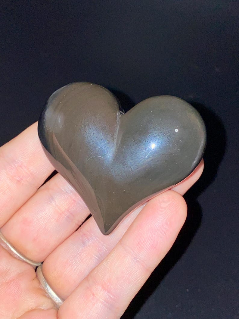 Puede incluir: Una piedra de obsidiana en forma de coraz&oacute;n de color gris oscuro con un ligero brillo iridiscente.