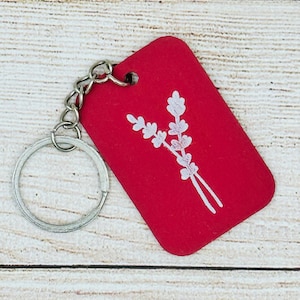 May include: A red keychain with a white floral design. The keychain is made of wood and has a silver metal ring.