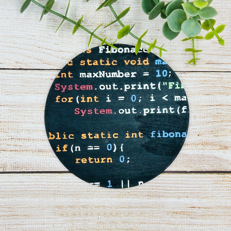 Op de afbeelding: Een zwarte cirkel met witte tekst die "Fibona static void main int maxNumber = 10; System.out.print("Fil for(int i = 0; i < ma System.out.print(f. blic static int fibona if (n == 0) { return 0; 1" zegt.