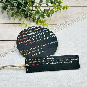 Op de afbeelding: Twee zwarte onderzetters met witte tekst. De grotere onderzetter heeft code voor een Fibonacci-sequentiefunctie. De kleinere onderzetter heeft code voor een "Hola Mundo"-functie.