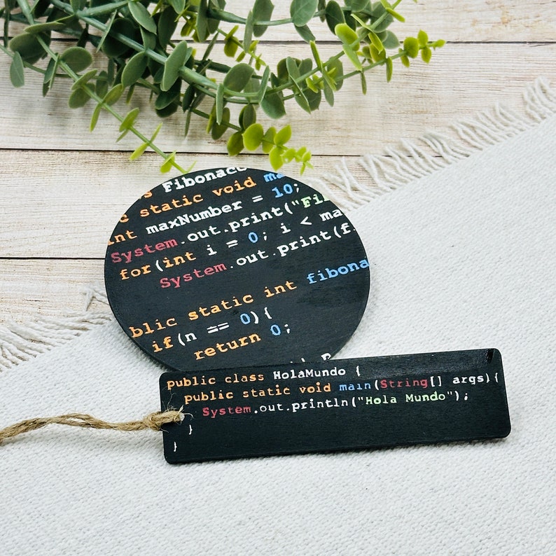 Op de afbeelding: Twee zwarte onderzetters met witte tekst. De grotere onderzetter heeft code voor een Fibonacci-sequentiefunctie. De kleinere onderzetter heeft code voor een "Hola Mundo"-functie.