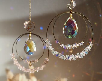 May include: Two hanging suncatchers with gold-colored metal rings and chains. Each suncatcher features a large, iridescent crystal teardrop pendant and smaller crystals. One has a star accent, the other a heart.