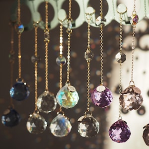 May include: A collection of crystal ball ornaments hanging from gold chains. Each ball is a different colour, including clear, purple, blue, and iridescent. The balls are labelled with Roman numerals.