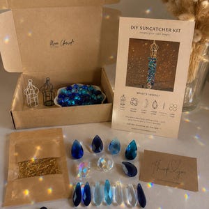 May include: A DIY suncatcher kit in a cardboard box containing blue and clear crystal beads, two small metal cages, a gold-tone chain, and jump rings. Includes an instruction card titled DIY SUNCATCHER KIT and a small thank you note.
