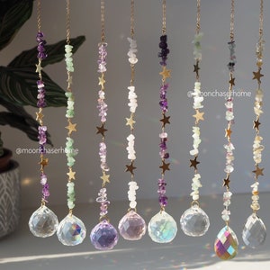 May include: Eight crystal suncatchers with gold chains and stars. Each suncatcher features a different combination of amethyst, green aventurine, and clear quartz crystals. The suncatchers are hanging from a white background.