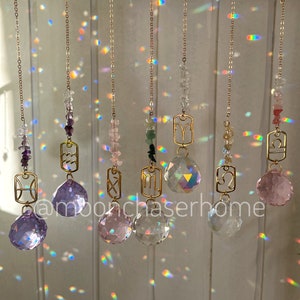 May include: Seven gold-toned zodiac sign charms hanging from chains with crystal prisms. The signs are: Pisces, Aquarius, Capricorn, Sagittarius, Scorpio, Libra, and Aries. The charms are strung with various coloured beads.