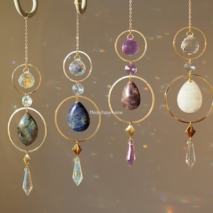 Peut inclure: Quatre ornements en cristal suspendus dorés avec des pierres précieuses de différentes couleurs. Chaque ornement présente une pierre précieuse en forme de larme, une petite boule de cristal et une plus grande boule de cristal. Les pierres précieuses sont l'améthyste, le blanc, le lapis-lazuli et le labradorite.