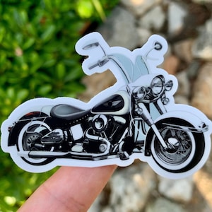 May include: A white and black motorcycle sticker with a white background and a black motorcycle with chrome accents. The motorcycle has a long, straight handlebar and a large, round headlight.