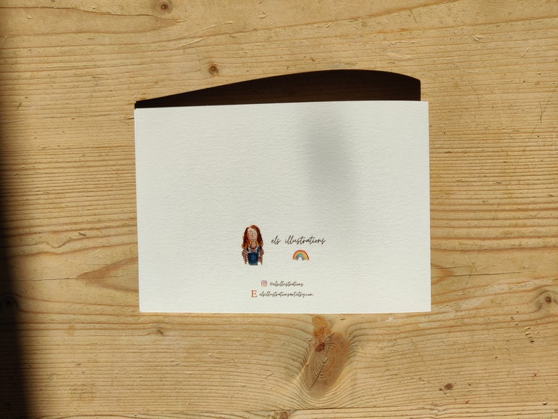 May include: A blank white card with a small illustration of a person with red hair and a rainbow. The text "els illustrations" is written below the illustration.