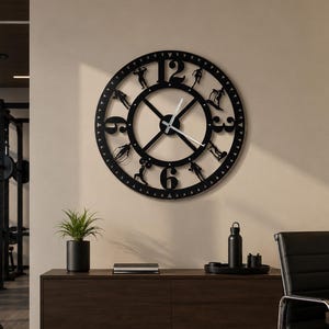 May include: A large circular black wall clock featuring cut-out silhouettes of people performing various fitness exercises between the numbers. The clock has a central cross design with white hour and minute hands, mounted on a light-colored wall.
