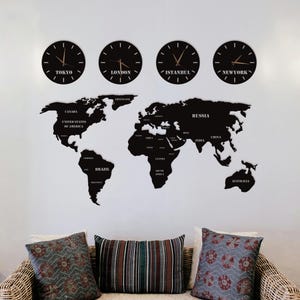 May include: A black world map wall decor with the names of countries and cities. Four black clocks above the map display the time in Tokyo, London, Istanbul, and New York. The decor is mounted on a white wall above a wicker sofa with decorative pillows.