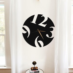 Puede incluir: Un reloj de pared negro moderno con números blancos a las 12, 3, 6 y 9 en punto. Las manecillas del reloj son doradas. El reloj es circular con diseños recortados. El reloj está montado en una pared blanca.