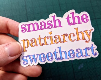 May include: A white sticker with the text "smash the patriarchy sweetheart" in purple, orange, and blue, with a small heart. The sticker has a scalloped edge.
