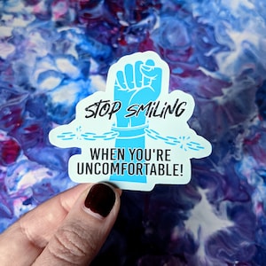 May include: A blue sticker with a raised fist in chains and the text "Stop smiling when you're uncomfortable!"
