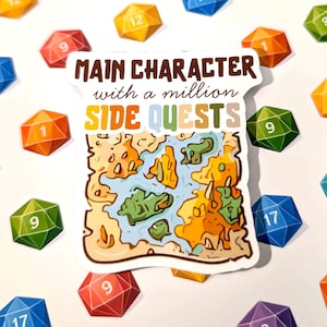Könnte beinhalten: Ein Aufkleber mit dem Text "MAIN CHARACTER with a million SIDE QUESTS" über einem Kartendesign. Bunte, vielseitige Würfel mit Zahlen wie 9, 12 und 17 sind verstreut. Der Aufkleber hat einen weißen Rand.