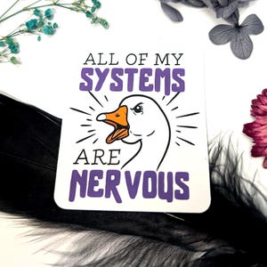 Könnte beinhalten: Ein weißer Aufkleber mit einer Cartoon-Gans-Illustration und dem Text "ALL OF MY SYSTEMS ARE NERVOUS" in Lila und Schwarz. Die Gans hat einen orangefarbenen Schnabel und strahlenförmige Linien.