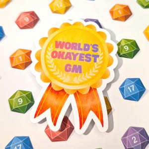 May include: A sticker with a yellow and orange ribbon design, featuring the text "WORLD'S OKAYEST GM" in purple and white. Scattered around are colourful, gem-shaped dice with numbers.