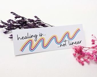 May include: White sticker with the text "healing is... ...not linear" in black cursive font. A colorful wavy line is drawn in yellow, pink, and blue.