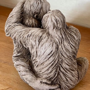 Può includere: Una scultura in cemento grigio di due scimmie che si abbracciano. Le scimmie sono sedute e hanno una pelliccia dettagliata.
