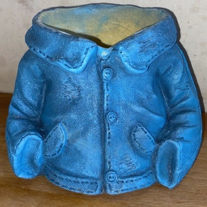 Könnte beinhalten: Ein blauer Keramik-Pflanztopf in Form einer Jeansjacke mit drei Knöpfen und zwei Taschen.