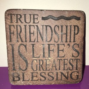 May include: A brown wooden sign with the text "TRUE FRIENDSHIP IS LIFE'S GREATEST BLESSING" in black lettering.