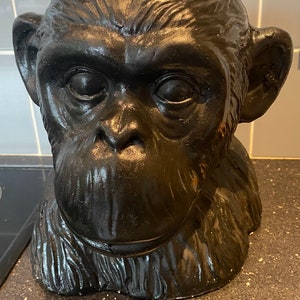 May include: A black ceramic sculpture of a chimpanzee head. The sculpture is detailed with fur and facial features.