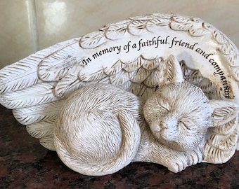 May include: White ceramic figurine of a sleeping cat with angel wings. The figurine has the inscription "In memory of a faithful friend and companion".