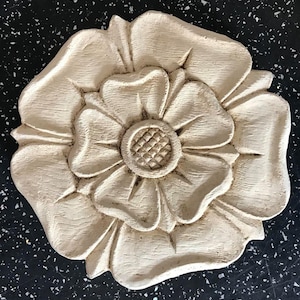 Puede incluir: Una flor de madera tallada blanca con un centro elevado y cinco pétalos. La flor es un elemento decorativo, posiblemente para una pared o un techo.