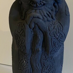 Può includere: Una scultura di gnomo in ceramica nera con un cappello a punta e una barba. Lo gnomo indossa una tunica con intricati disegni di nodi celtici.