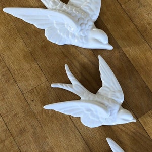 Puede incluir: Tres piezas de decoración de pared de golondrina de cerámica blanca en varios tamaños. Los pájaros están en posición de vuelo con las alas extendidas.