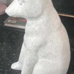 May include: A white ceramic polar bear figurine sitting on a black surface. The bear is sitting with its head tilted down and its eyes closed.