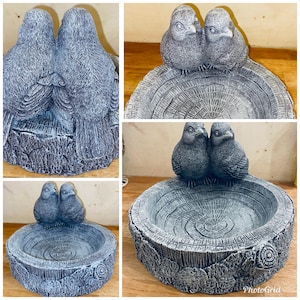 Puede incluir: Un bebedero gris con dos pájaros pequeños posados en el borde. El bebedero está diseñado para parecerse a un tocón de árbol con una cuenca circular. Los pájaros miran hacia adelante y el diseño es detallado.