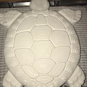Puede incluir: Escultura de tortuga de cerámica blanca con un diseño de caparazón detallado. La tortuga está tumbada de espaldas con las patas y la cabeza visibles.
