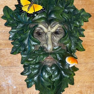 Könnte beinhalten: Eine grüne Männergesichts-Skulptur mit einem gelben Schmetterling und einem Pilz an der Seite. Die Skulptur ist aus Harz gefertigt und detailliert gestaltet.