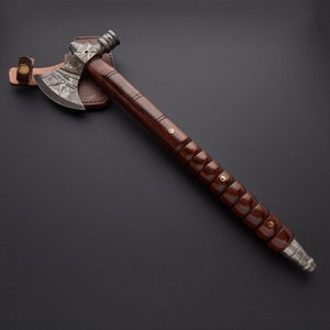 May include: A hand-forged tomahawk with a dark wood handle and a leather sheath. The head of the tomahawk is made of steel and has a hammered finish.