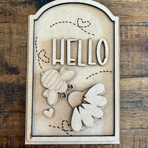 May include: Wooden sign with a cutout of a bee and a flower. The sign says "HELLO" in a decorative font.