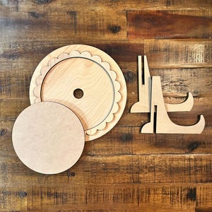 May include: Unfinished wooden cake stand kit with a scalloped edge, a smaller round base, and two support stands. The pieces are made of light-colored wood and are ready to be painted or decorated.