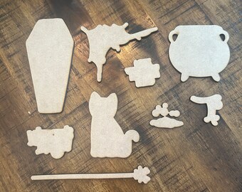May include: A set of nine wooden Halloween-themed cutouts, including a coffin, a cauldron, a cat, a wand, a splattered paint design, a paw print, a broom, and two other shapes.