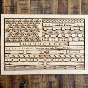 May include: A wooden American flag design with the words "We the People of the United States, in Order to form a more perfect Union, establish Justice, insure domestic" and "USA" along with the year "1776" repeated twice.
