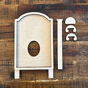 May include: Unfinished wooden sign with an arched top, an oval cutout, and a rectangular base. The sign is accompanied by separate wooden pieces, including a long vertical piece and two curved pieces, likely for assembly. The wood has a natural, light color.