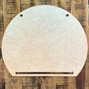 May include: A plain, unfinished, light brown wooden half-circle with two holes at the top and a slot at the bottom. The half-circle is perfect for crafting and DIY projects.