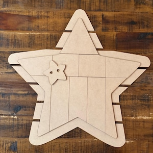 May include: A large, unfinished wooden star with a smaller star cutout attached. The star is divided into rectangular sections and has a layered design. The wood has a natural, light brown color.