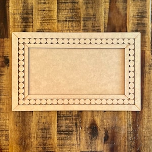 May include: A wooden picture frame with a beaded border. The frame is light brown and has a rectangular shape.
