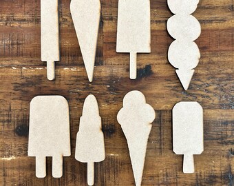 May include: A collection of eight unfinished wooden cutouts in the shapes of ice cream treats, including popsicles and ice cream cones. The cutouts are arranged on a dark wooden surface, showcasing their natural wood grain.