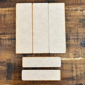 May include: Five unfinished wooden rectangular shapes, three tall and two shorter, arranged in a row on a brown wooden surface.