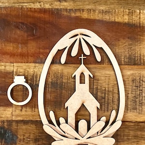 May include: Wooden cutout of an Easter egg with a church inside. The egg is decorated with a floral design and a cross on top of the church. There is a separate wooden ring included.