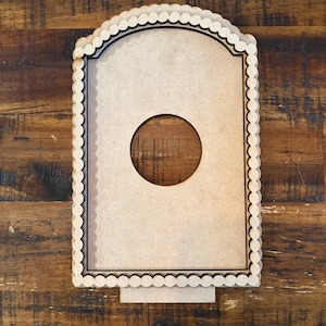 May include: A light brown, rectangular wooden frame with a circular cutout and scalloped edges. The frame has a black border and a small rectangular base. The wood grain background adds a rustic touch.