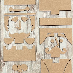 May include: A set of wooden nutcracker craft pieces. The pieces are in various shapes and sizes, including the head, hat, mustache, and body. The pieces are all brown and have a rustic look.